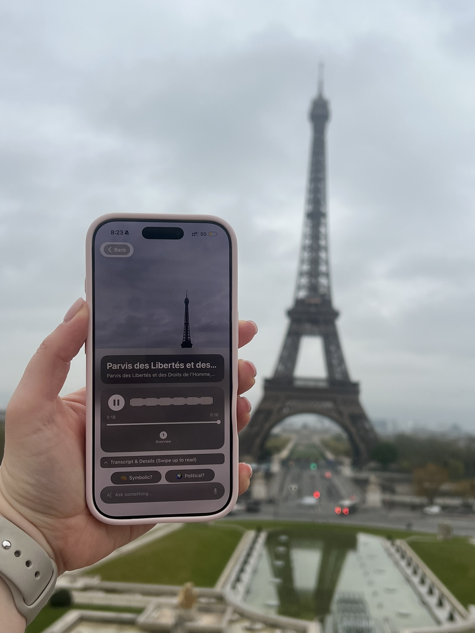 Chiaro running on a phone held up in front of the Eiffel Tower in Paris, the audio guide playing while the real tower is visible behind the screen.