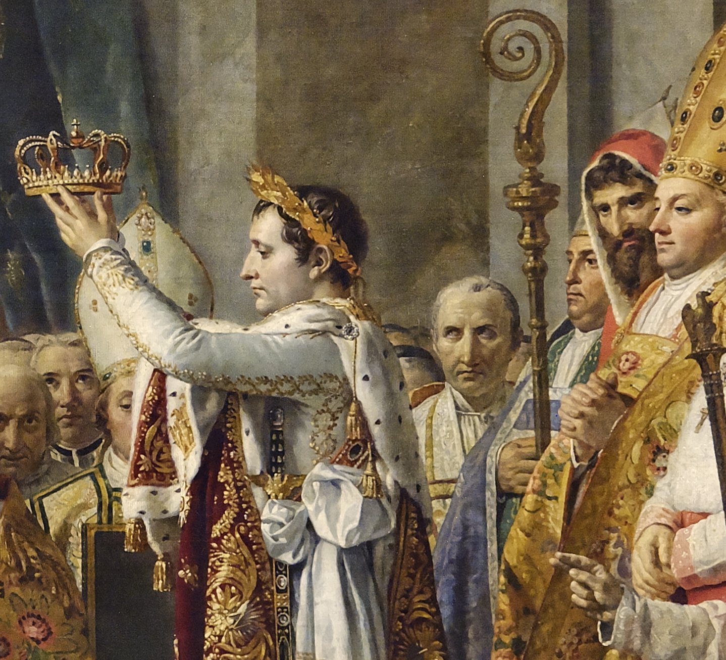 Close detail of Napoleon holding the crown aloft, and just to his right a grey-faced, grey-haired priest who lifts his eyes toward the emperor, beside a bearded man in a red hood and a mitred bishop.