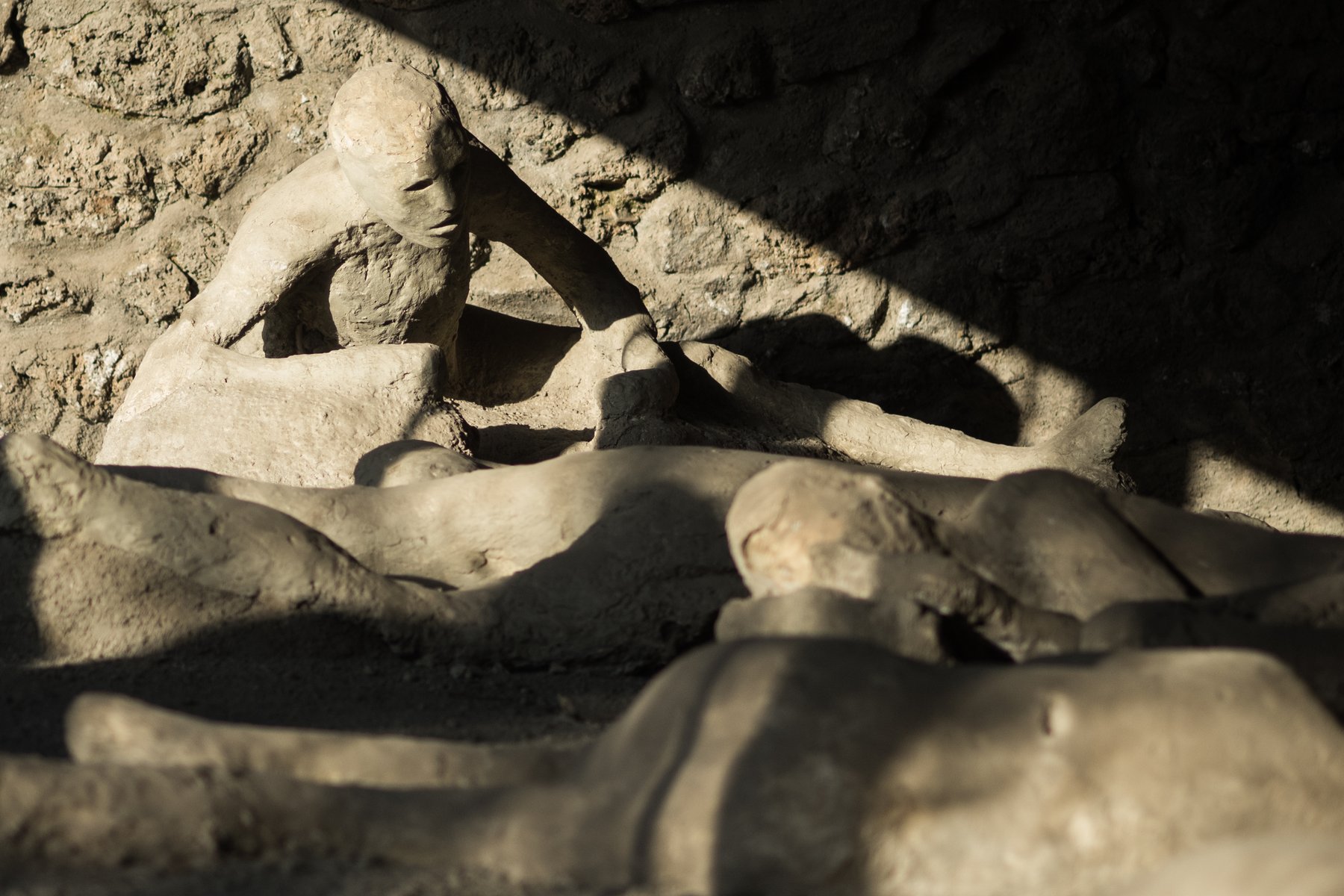 A plaster cast of a body of one of the eruption victims of Pompeii, lying curled on a low pedestal, with the form of cloth and limbs preserved in the ash impression.
