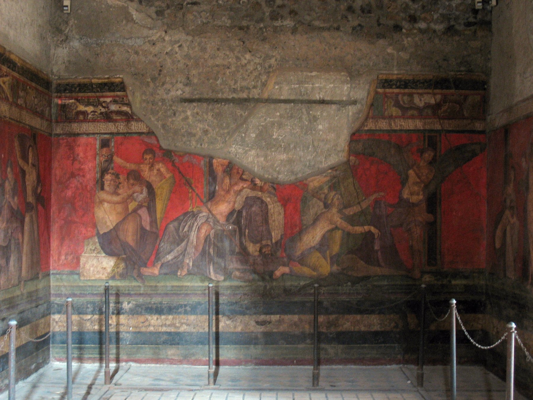 A wall of the Villa of the Mysteries in Pompeii, painted with a fresco of figures in red-grounded Roman fresco style enacting a Dionysian initiation scene.